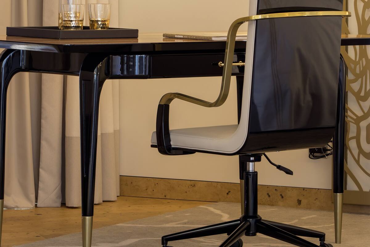 A modern office chair with wheels, a desk with a laptop, a glass pitcher, and two glasses on a tray.