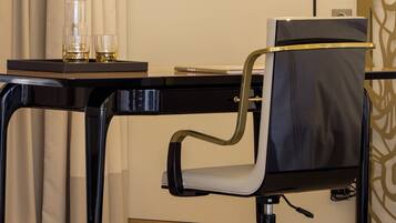 A modern office chair with wheels, a desk with a laptop, a glass pitcher, and two glasses on a tray.