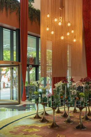 A lobby with large windows, a red curtain, and a series of vases with flowers on a patterned carpet.