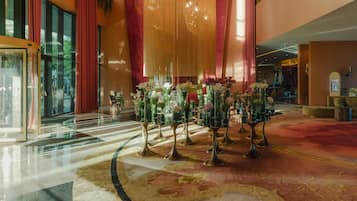A spacious lobby with a high ceiling, a large chandelier, and a central floral arrangement.