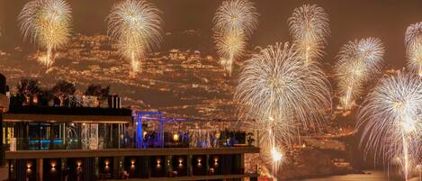 A hotel with multiple floors, balconies, and a view of fireworks over a body of water.