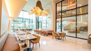 Ein modernes Restaurant mit einem langen Esstisch, gepolsterten Sitzgelegenheiten und einem großen Fenster mit Blick ins Freie.