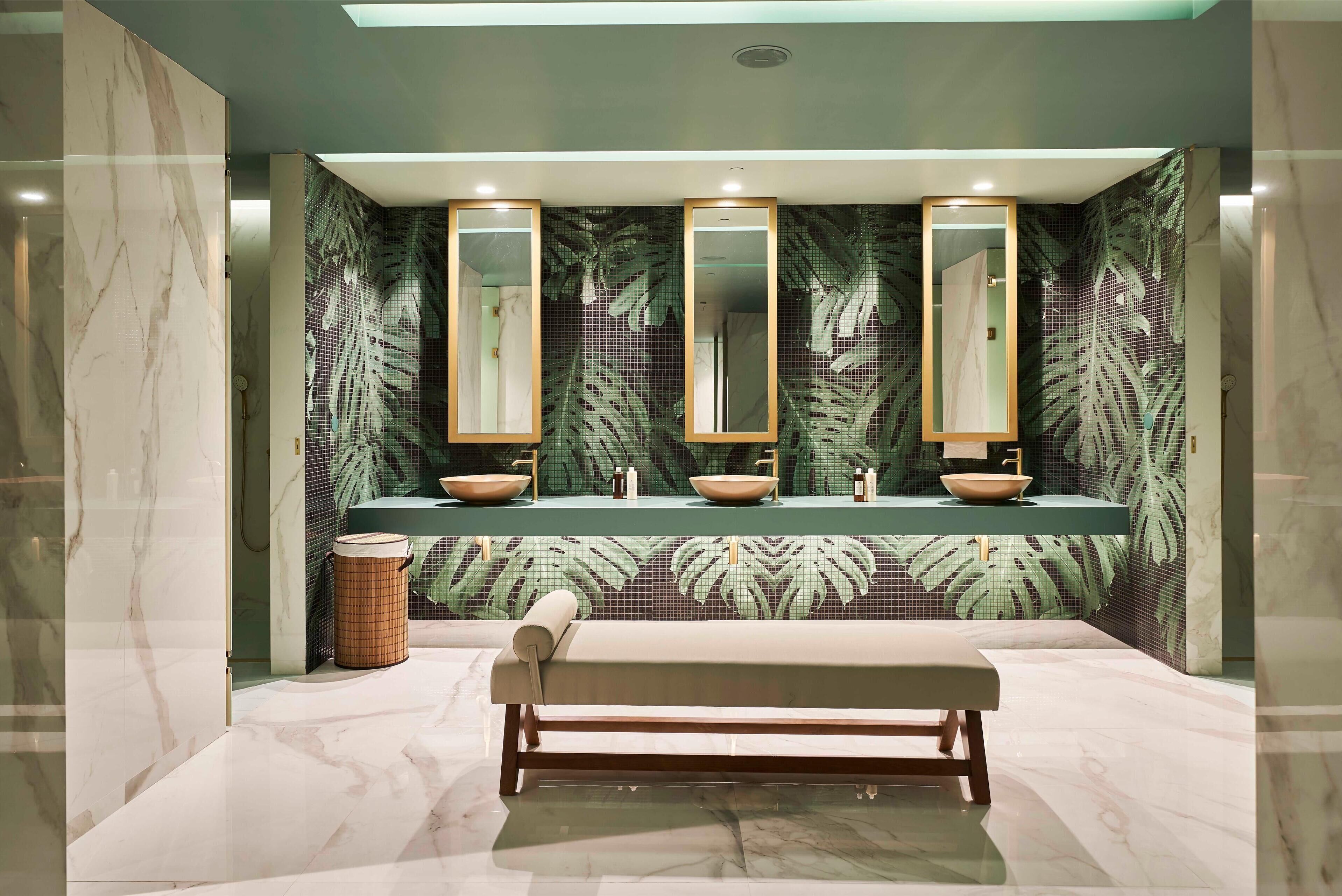 A modern bathroom with three sinks, large mirrors, and a bench.