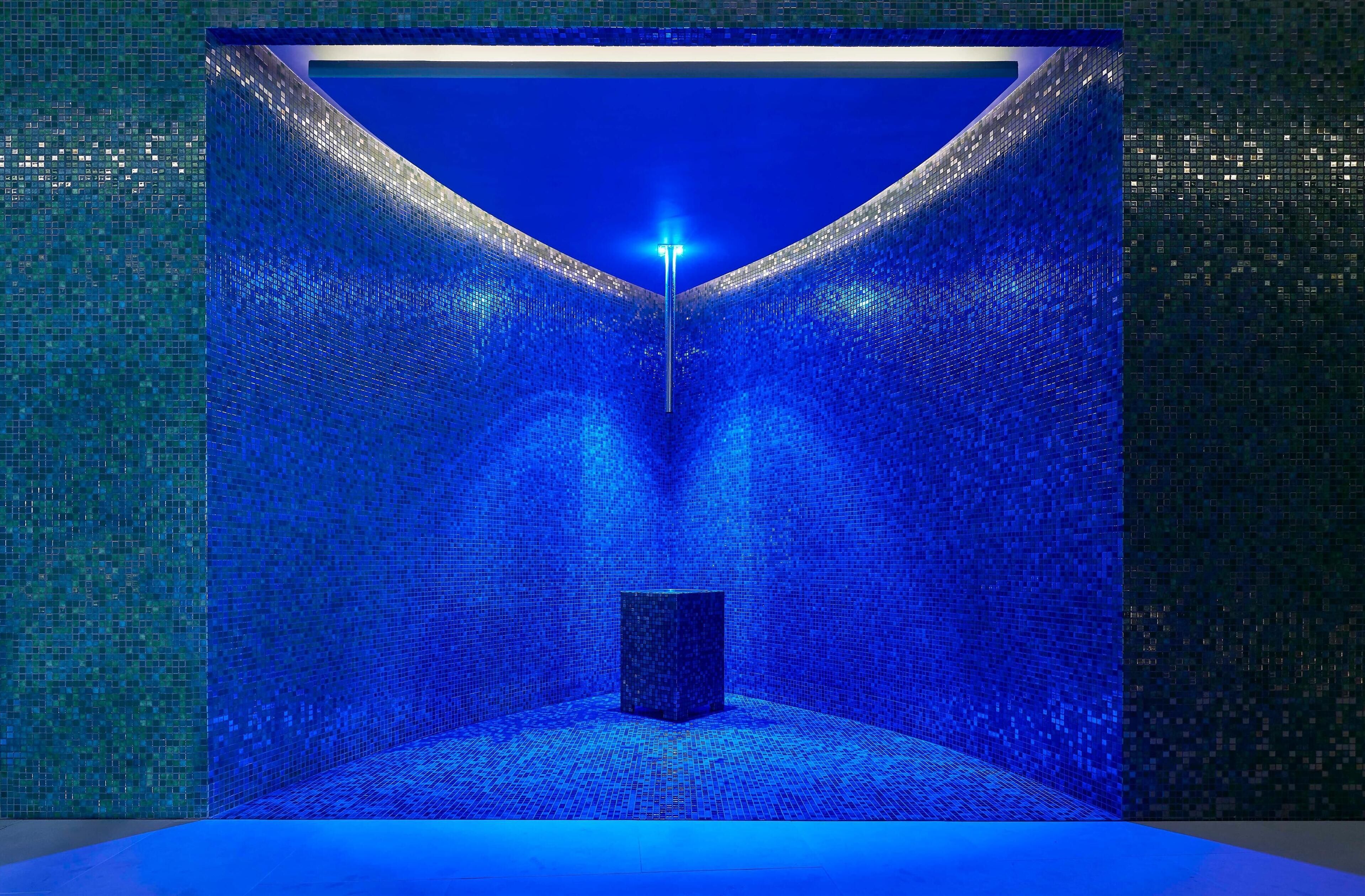A room with a tiled floor and walls, a central light fixture, and a dark cube structure.