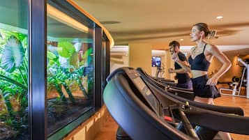 Une salle de sport équipée de tapis de course et d’appareils d’exercice, un grand aquarium rempli de poissons tropicaux et un écran de télévision en arrière-plan.