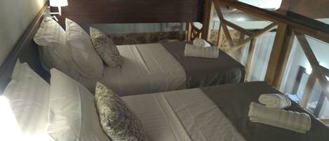 Una habitación acogedora con dos camas, cada una con almohada y manta. Tiene cabecera de madera y una ventana con cortinas.