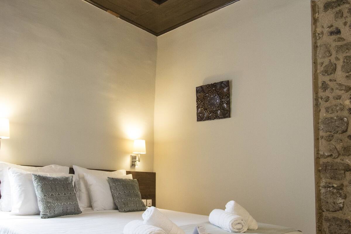 Un dormitorio con una cama grande, cabecero de madera, pared de piedra y un cuadro pequeño.