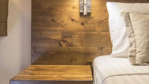 Ein hölzerner Kopfteil, eine Wandlampe, ein Nachttisch und ein Bett mit Kissen.