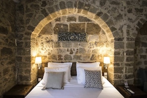 A stone-walled room with a bed, two bedside lamps, and a decorative plaque on the wall.