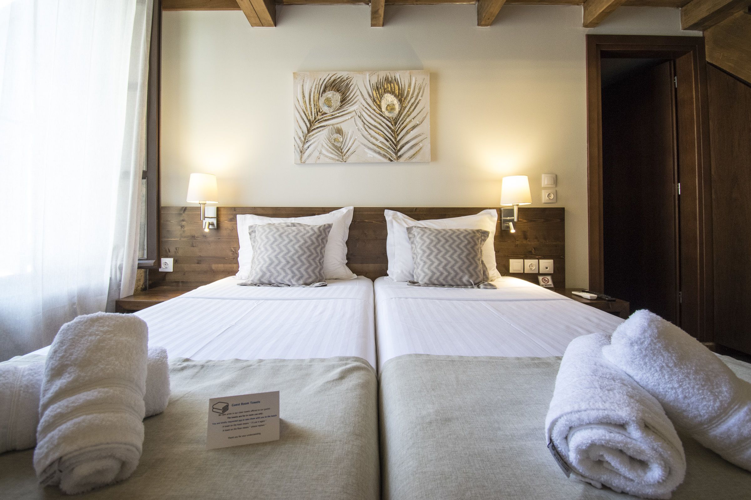 Habitación de hotel con dos camas, cada una con una almohada y una toalla enrollada. Encima de las camas hay una obra de arte en la pared y una lámpara a cada lado.