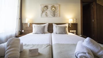 Habitación de hotel con dos camas, cada una con una almohada y una toalla enrollada. Encima de las camas hay una obra de arte en la pared y una lámpara a cada lado.