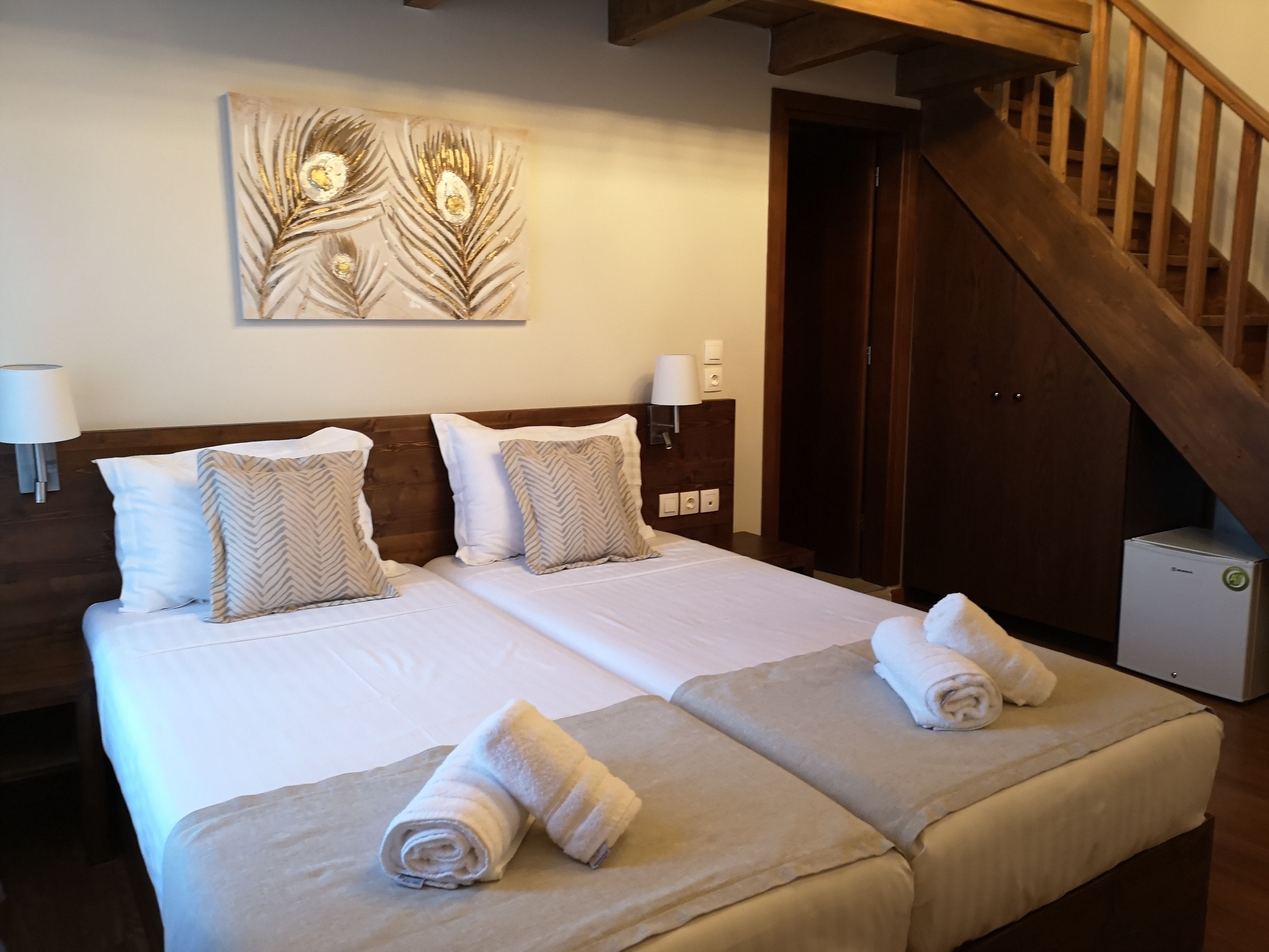A double bed with two pillows, a wall-mounted artwork, a nightstand with a lamp, and a wooden staircase.