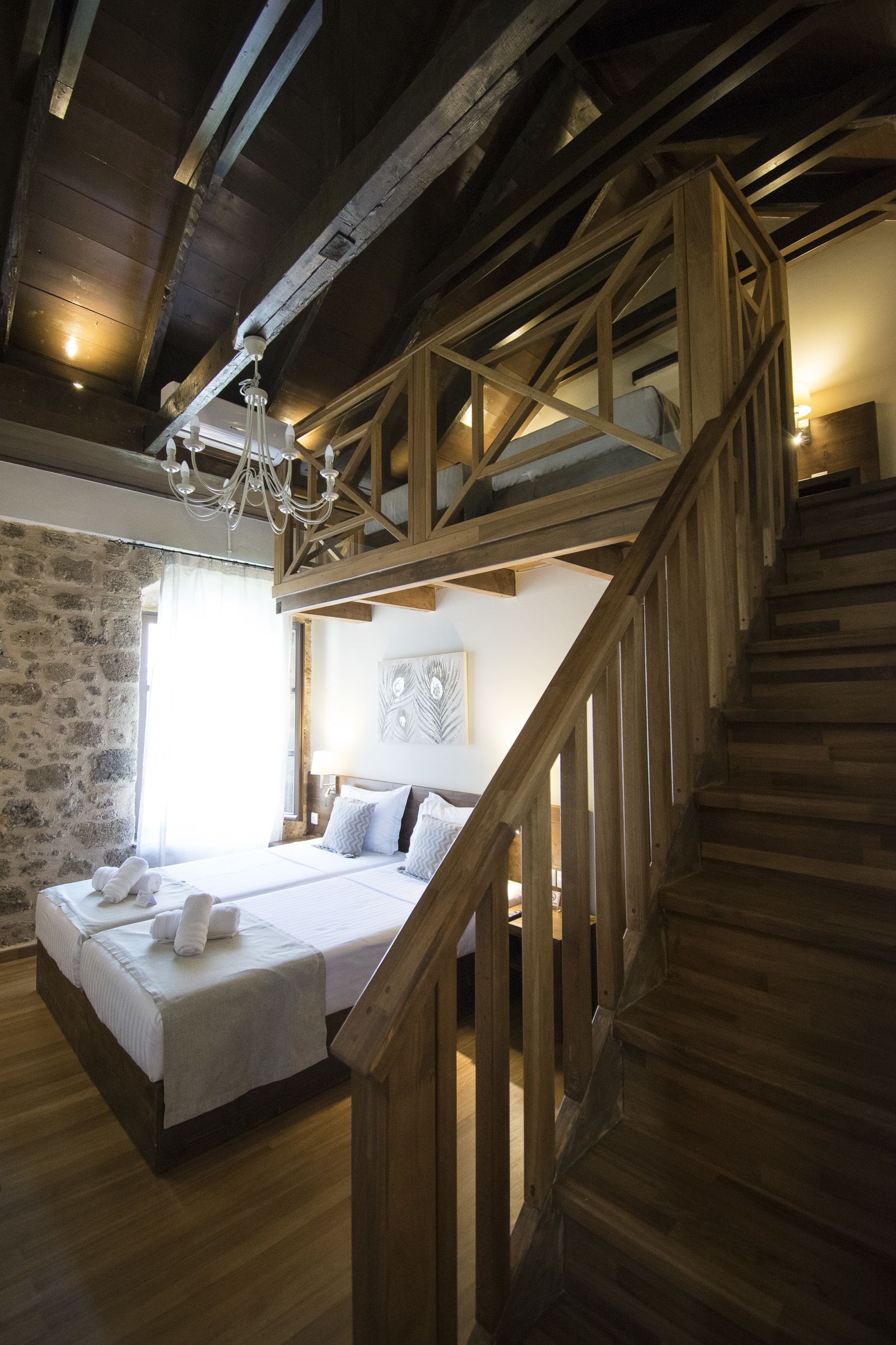 A bedroom with a wooden staircase, a bed with white linens, and a stone wall.