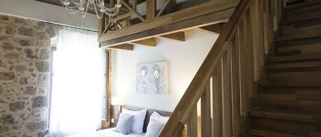 Un dormitorio con escaleras de madera, una cama con ropa blanca y una pared de piedra.