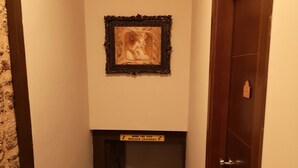 Een smalle gang met een houten deur aan de rechterkant, een trap die naar een hoger verdiep leidt, en een lijst met een afbeelding aan de muur.