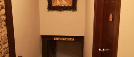 Un couloir étroit avec une porte en bois sur la droite, un escalier menant à l’étage supérieur et un tableau encadré accroché au mur.