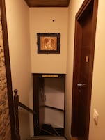 A narrow hallway with a wooden door on the right, a staircase leading to an upper floor, and a framed picture on the wall.
