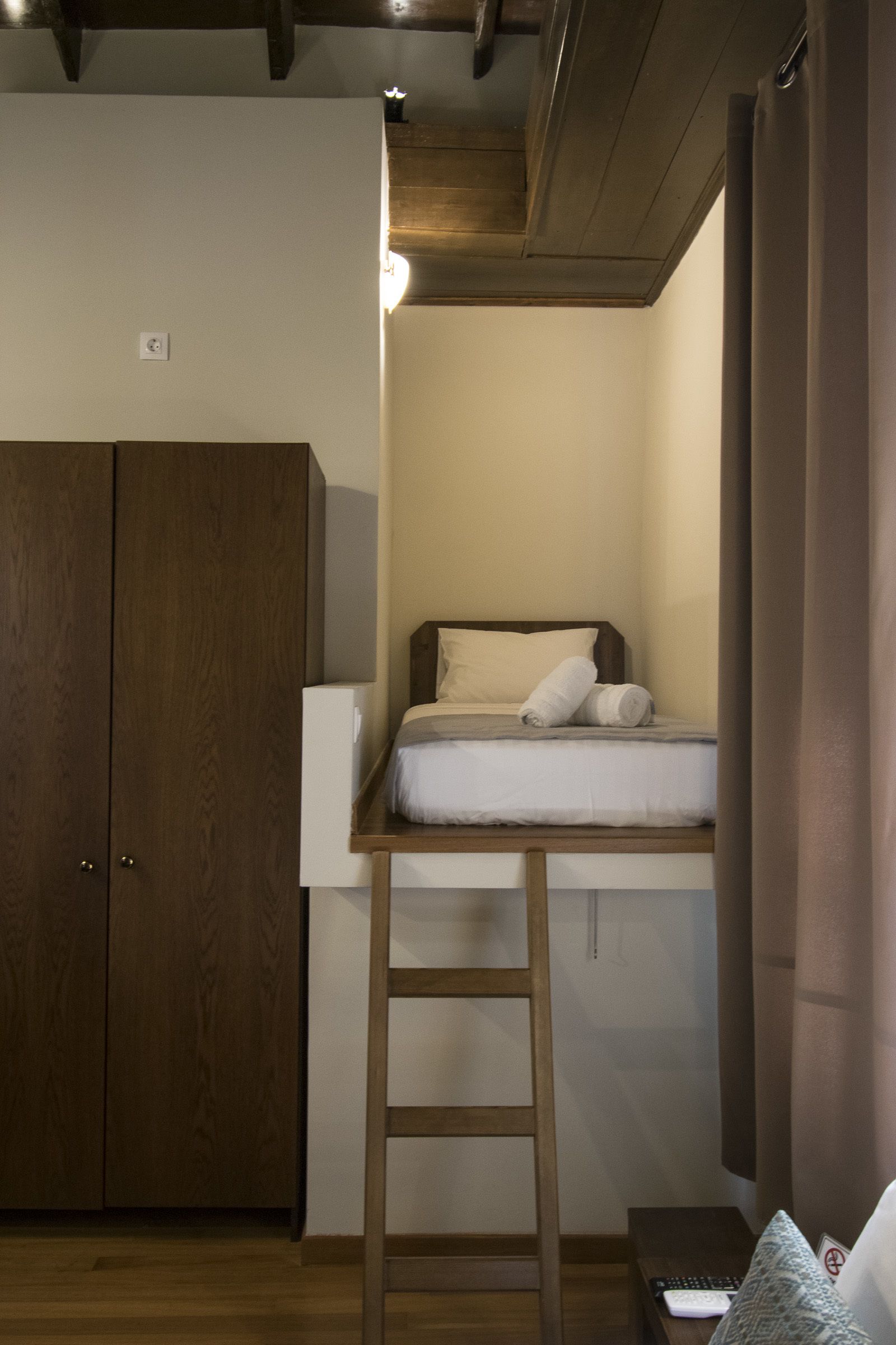 A bedroom with a loft bed, wooden wardrobe, and a ladder.