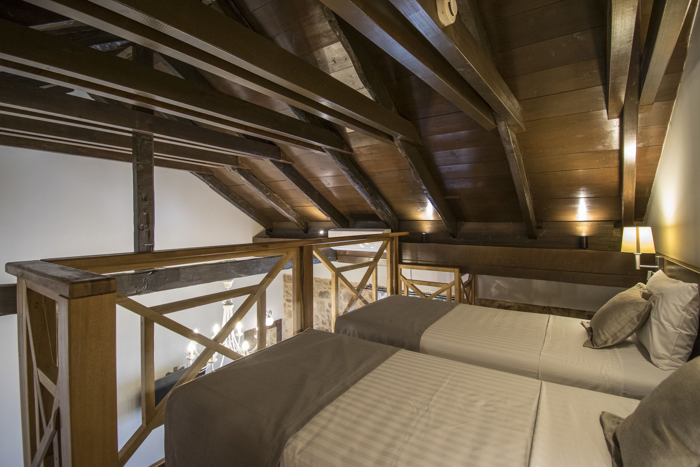 Ein Zimmer mit hohen Decken, Holzbalken, zwei Betten mit Kissen und einem kleinen Tisch.