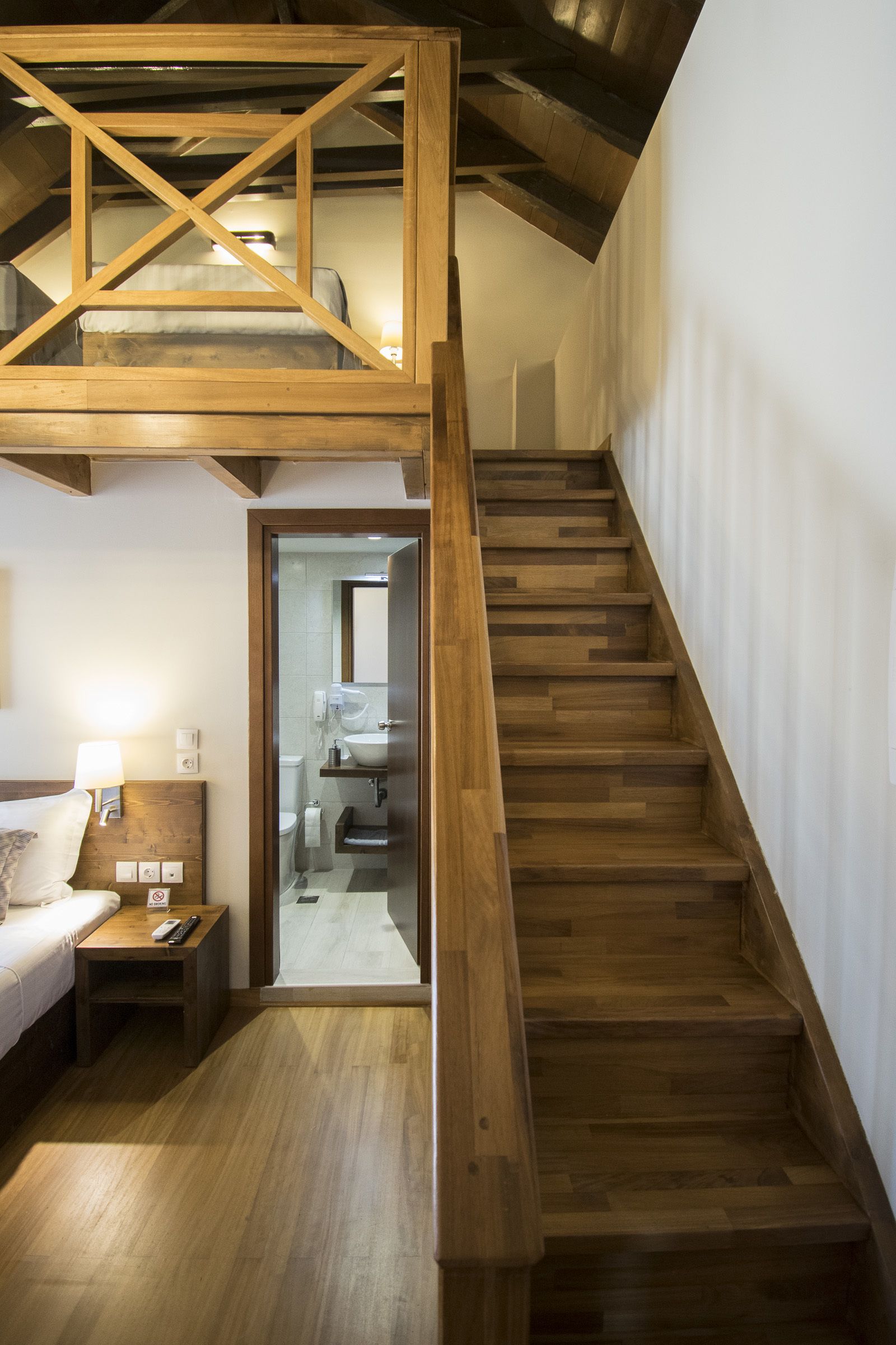Una escalera de madera que lleva a un nivel superior con una cama y una mesita de noche.