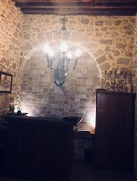 Egy kőfalas konyha, melyben egy csillár, fa szekrények és csempével borított fal található a munkalap felett.
