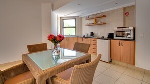 Una cocina moderna con comedor, que incluye una mesa de vidrio, sillas de mimbre y un florero con flores.
