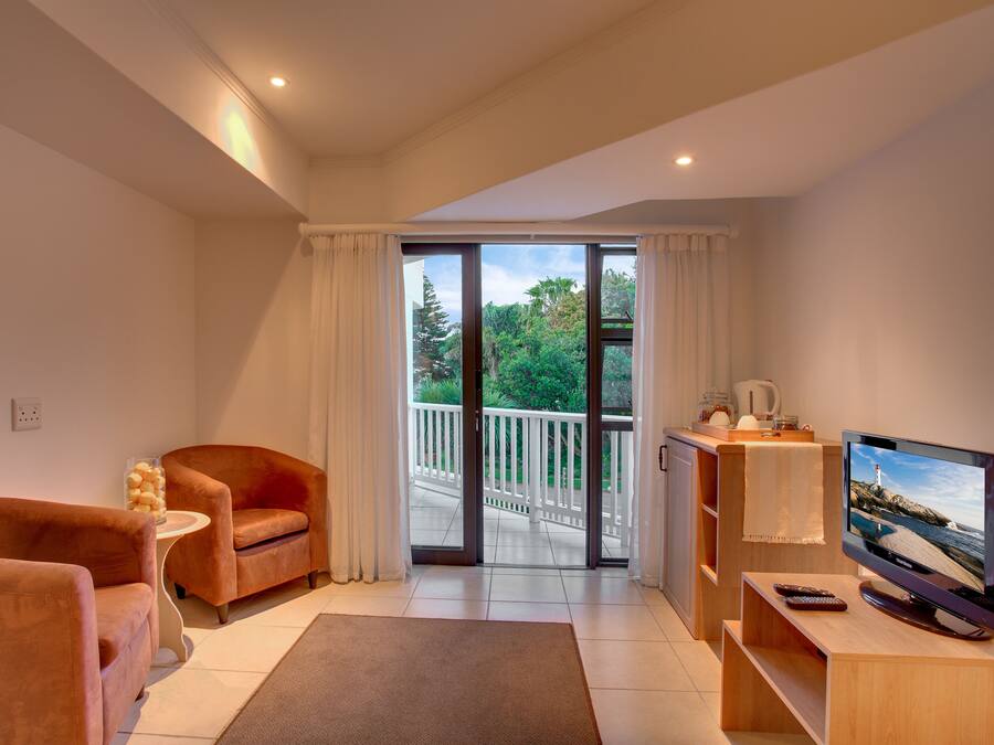 A modern living room with a sofa, a TV, and a balcony with a view of trees and a white fence.