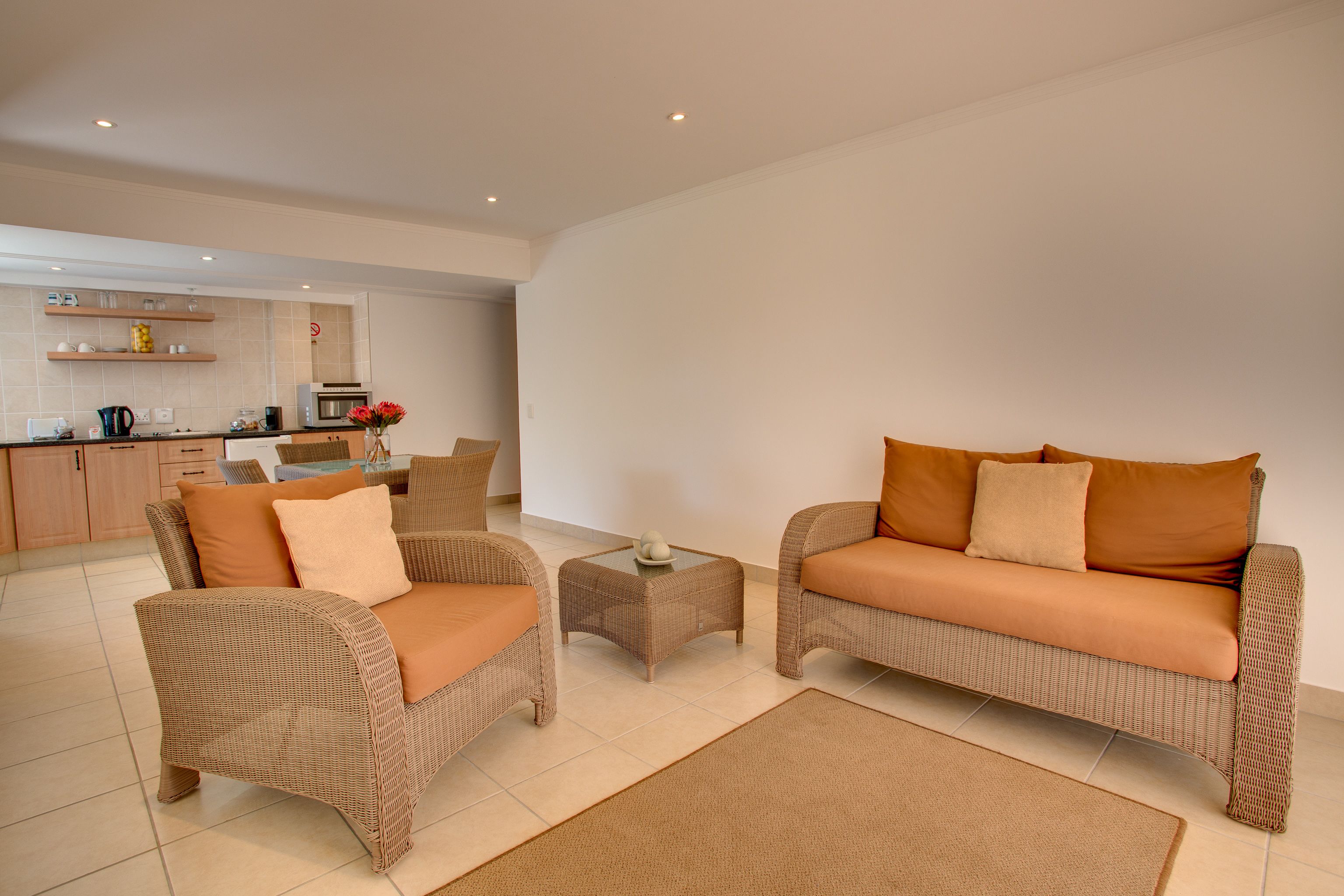 A modern living room with wicker furniture, a coffee table, and a kitchen in the background.