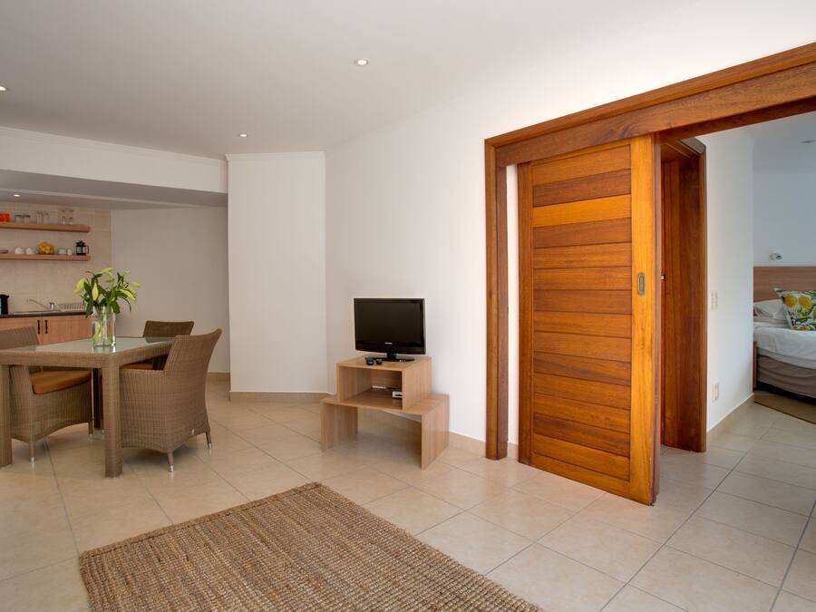 Uma sala de estar moderna com área de jantar, um rack para TV e uma porta de madeira que dá para um quarto.