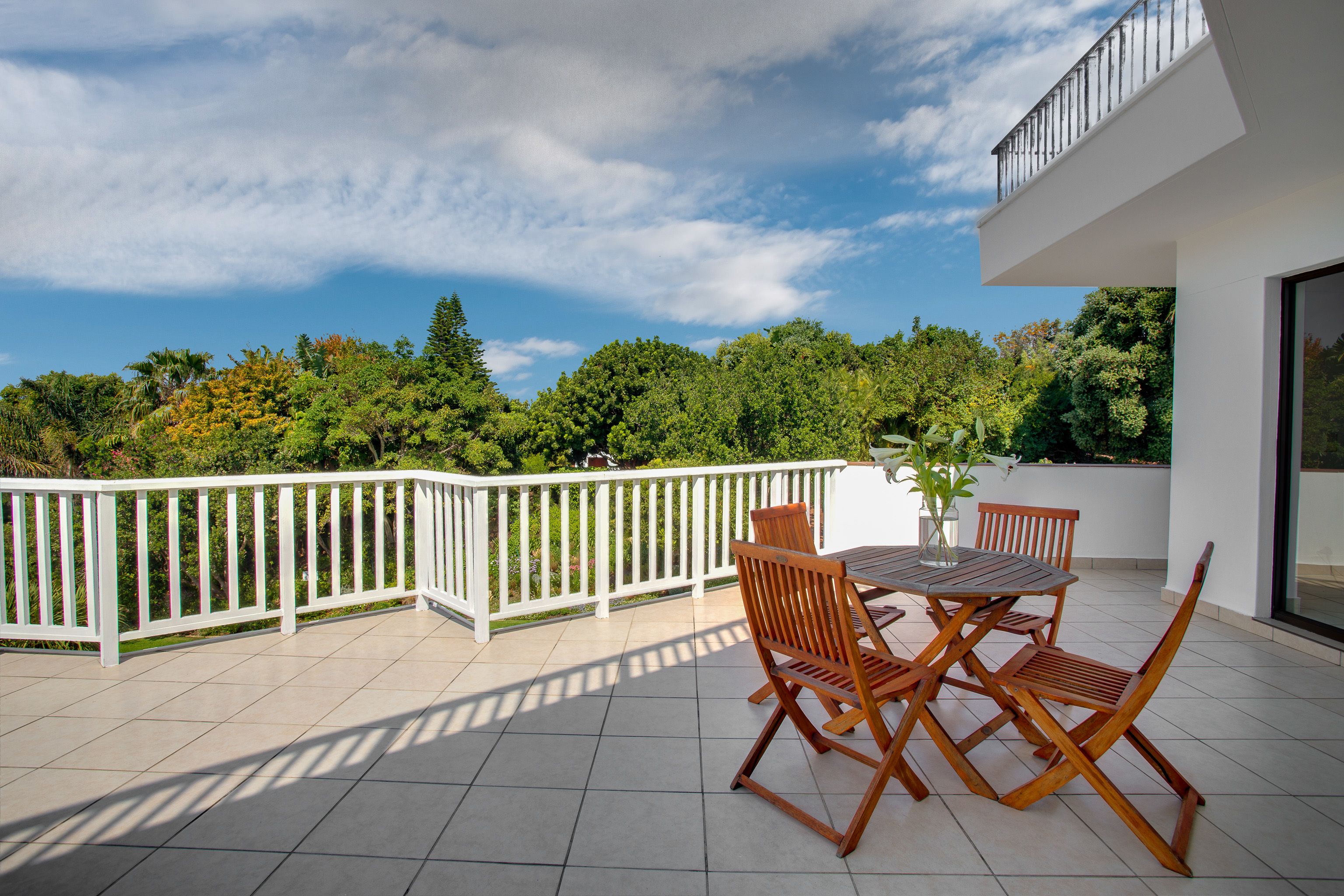 A balcony with a white railing, a wooden table, and two wooden chairs.