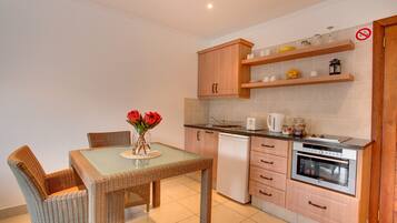 Una cocina moderna con una mesa de comedor, sillas de mimbre, horno empotrado y cafetera.