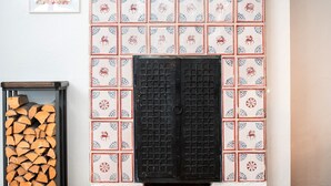 A fireplace with patterned tiles, a stack of firewood, and framed pictures on the wall. - Tuchhaus (Volkach)