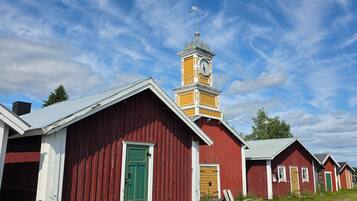 A row of red wooden buildings with a clock tower, featuring a green door and a weather vane.