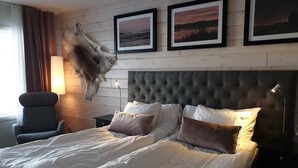 A hotel room with a large bed, a chair, a nightstand, and a wall-mounted lamp.