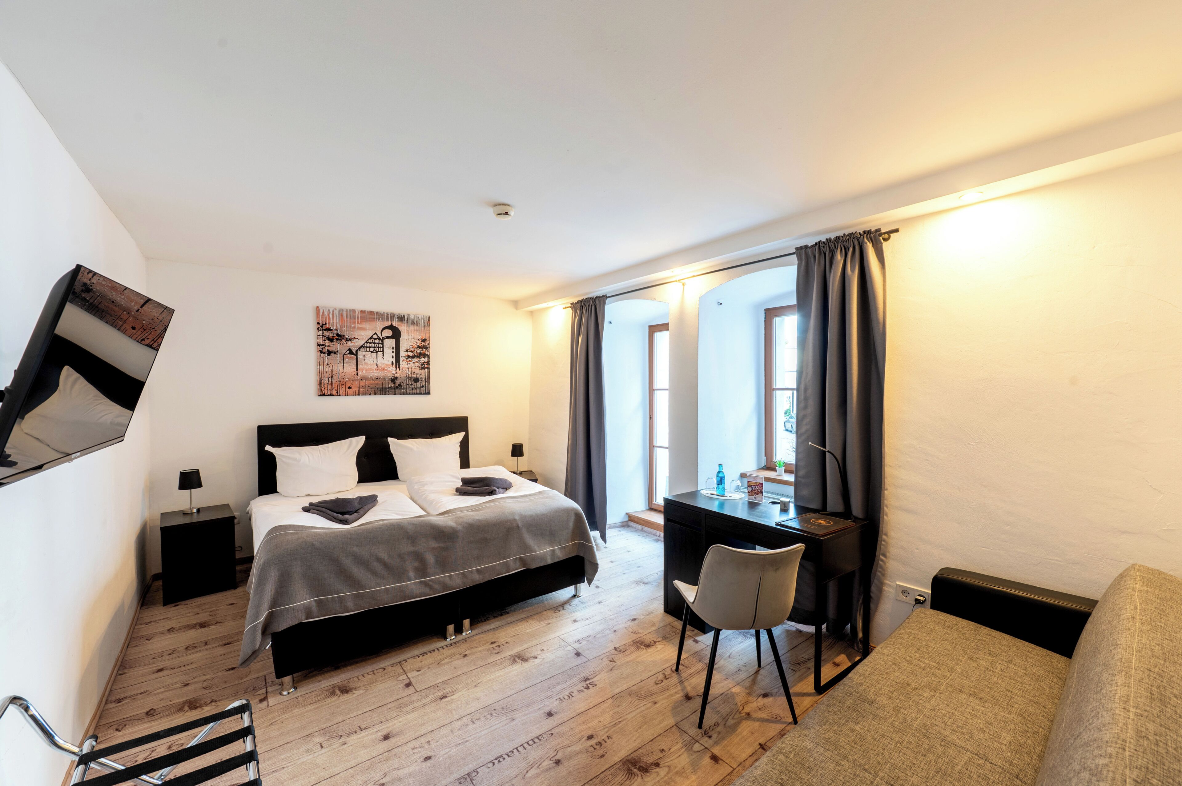 A bedroom with a bed, desk, chair, and artwork on the wall.