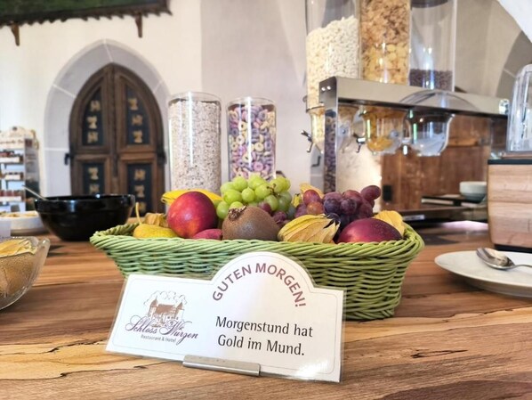 Un bufé de desayuno con una variedad de frutas y cereales, un letrero con el nombre del hotel y un interior rústico con puertas de madera.