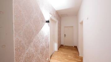 Un couloir avec un papier peint à motifs, un plancher en bois et des portes blanches.