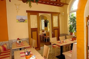 A restaurant with booths and tables, wooden beams, a brick wall, and a large potted plant.