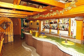 A bar area with a curved counter, shelves with bottles, and a tiled floor.