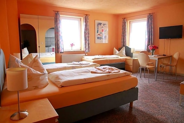 A hotel room with two beds, a desk, a chair, a TV, and a window with curtains.