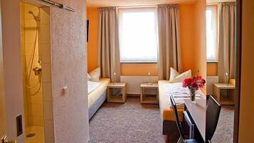 A hotel room with a bed, bedside tables, a desk, and a shower.