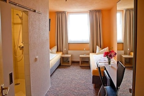A hotel room with a bed, bedside tables, a desk, and a shower.