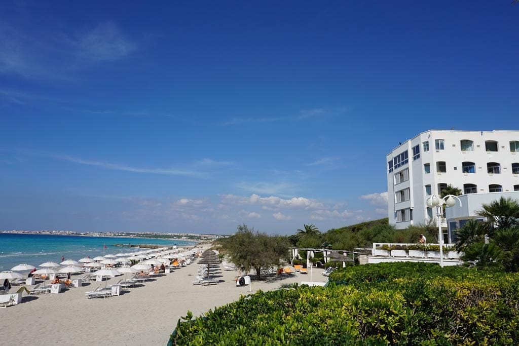 Un hotel frente a la playa con varios balcones, zona de piscina y vistas al mar.