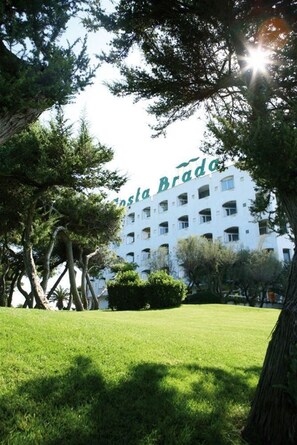 Un bâtiment dont on aperçoit partiellement l’inscription « Estal Brado », entouré d’arbres et d’une pelouse bien entretenue.