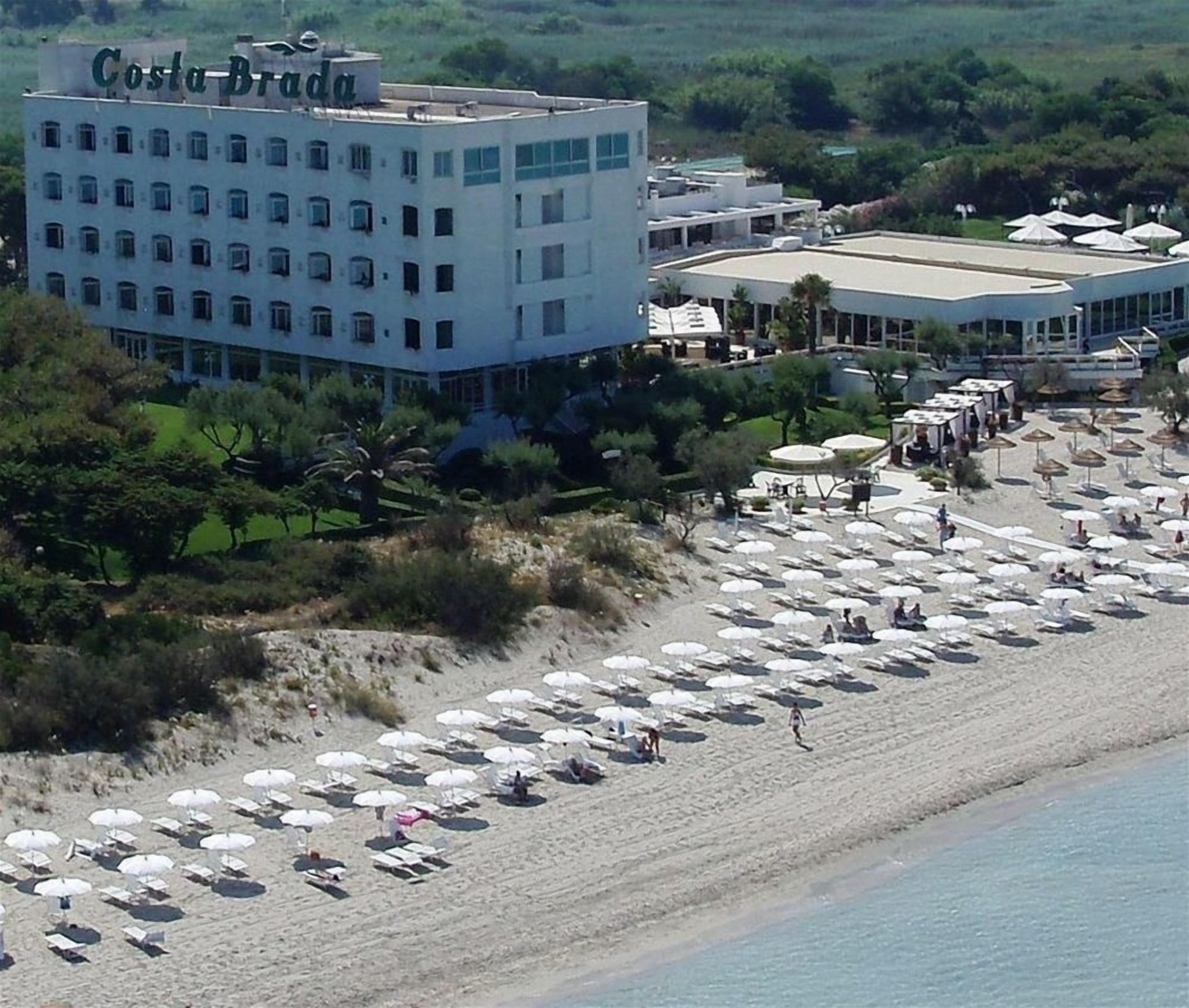 A hotel named Costa Brada with a beach area featuring numerous umbrellas and a few people.