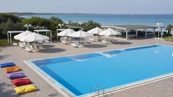 Una piscina con sillas de descanso y sombrillas, un área de estar cubierta y vistas al mar.