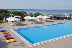 A swimming pool with lounge chairs and umbrellas, a covered seating area, and a view of the sea. - Costa Brada (Gallipoli)
