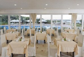 Un restaurant avec des tables dressées pour le service, donnant sur un espace piscine.