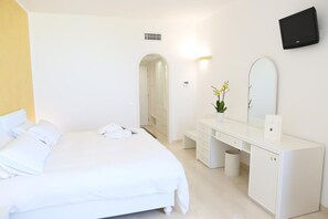 A hotel room with a large bed, a white dresser, a mirror, and a TV mounted on the wall.
