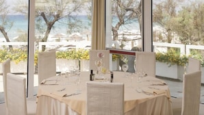 A dining table set for six with a view of the sea and trees through large windows. - Costa Brada (Gallipoli)